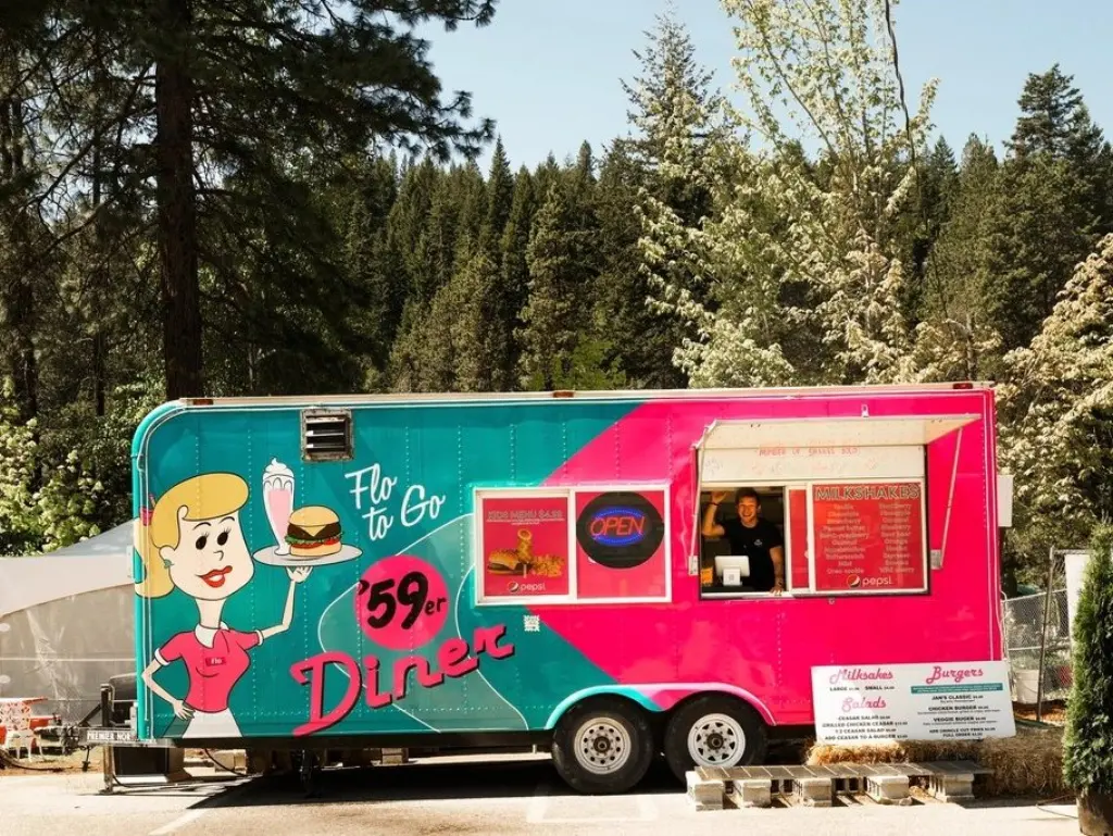 Colourful food truck parked by the woods with its window open