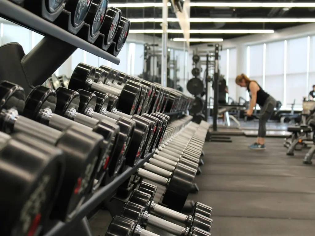 Rack of dumbbells on a gym floor, someone training in the back