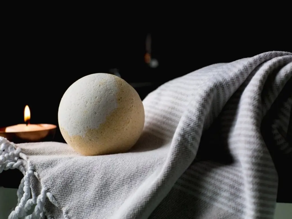 Folded towel, candle and bath bomb against a dark background